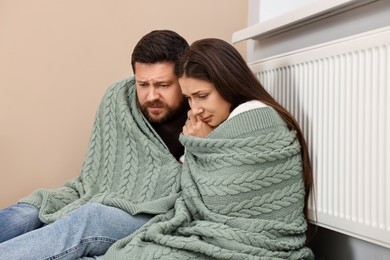 Couple with blanket warming up near heating radiator at home