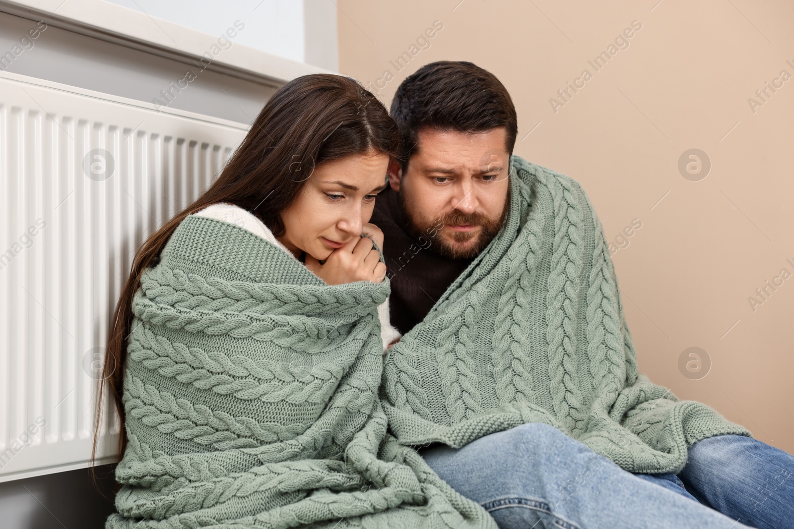 Photo of Couple with blanket warming up near heating radiator at home