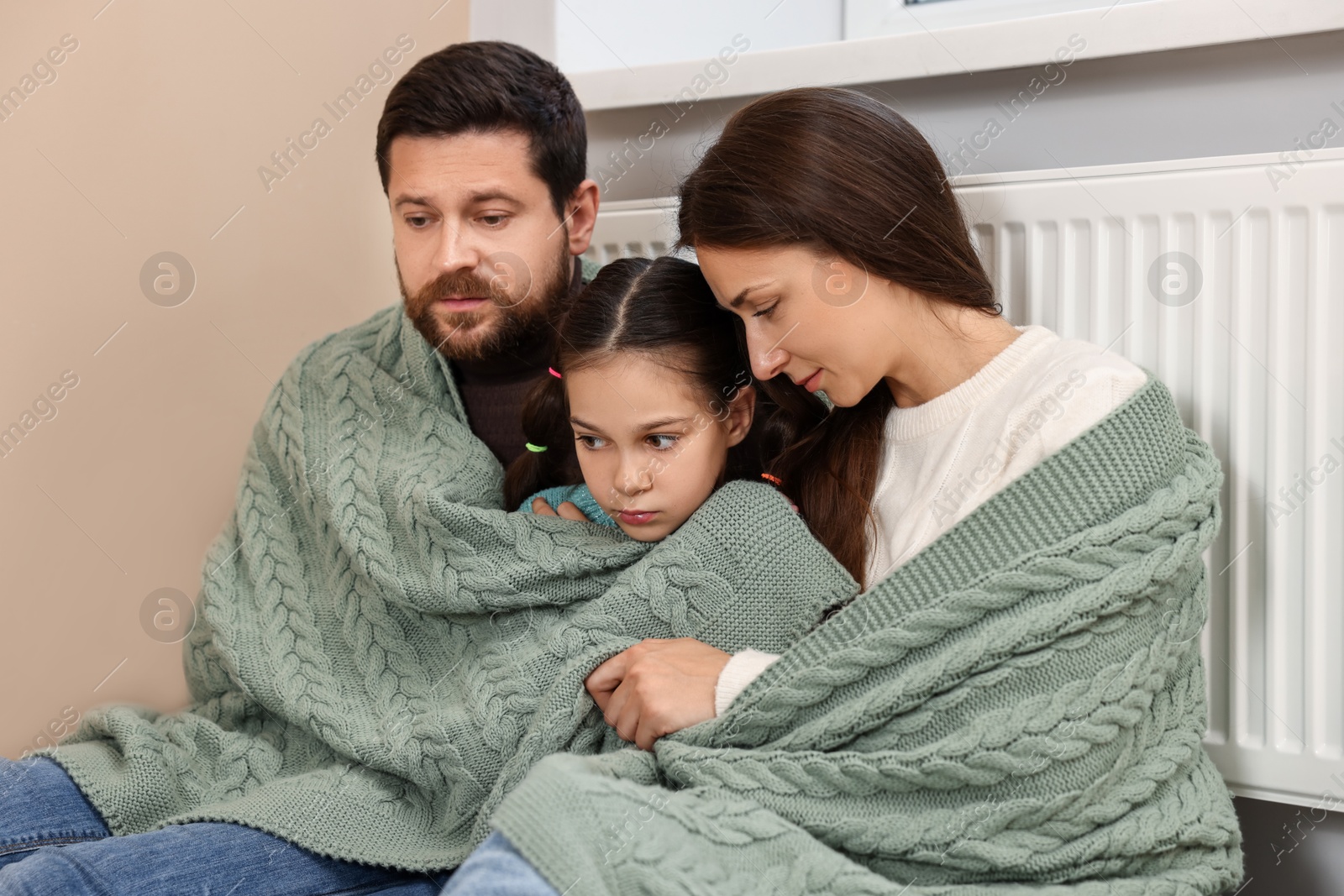 Photo of Family with blanket warming up near heating radiator at home