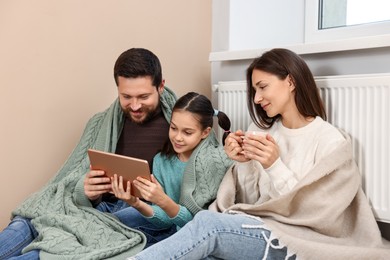 Happy family with tablet near heating radiator at home