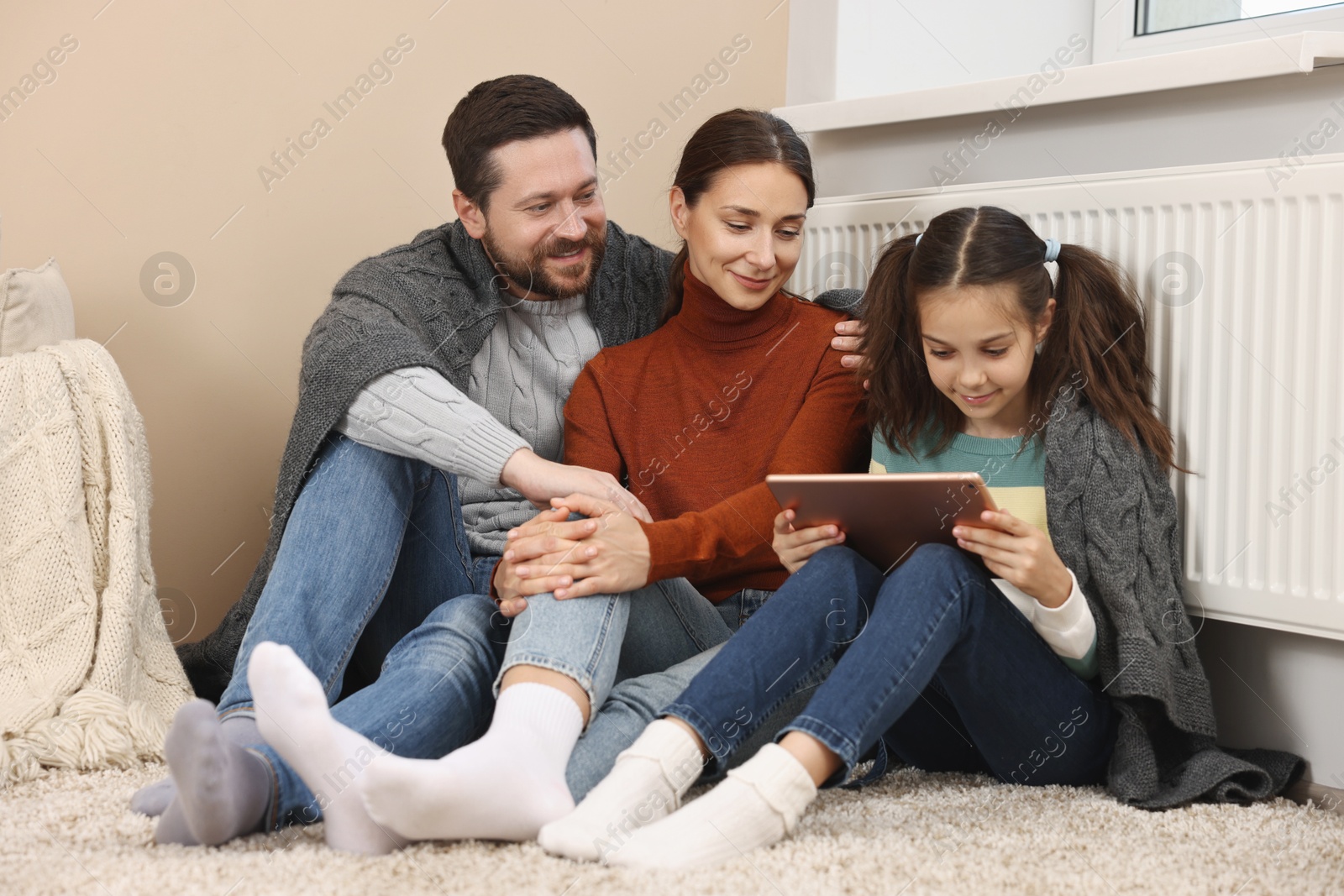 Photo of Happy family with tablet warming near heating radiator at home