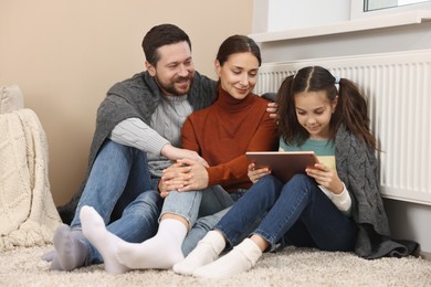 Happy family with tablet warming near heating radiator at home