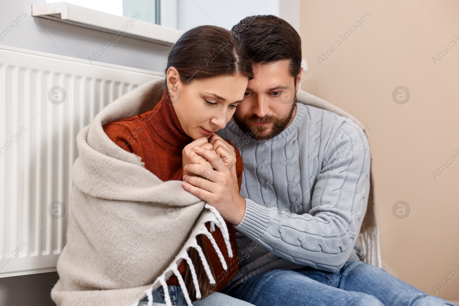 Photo of Couple with blanket warming up near heating radiator at home