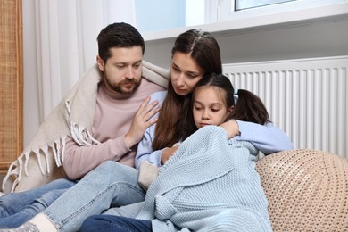 Photo of Family with blankets warming near heating radiator at home