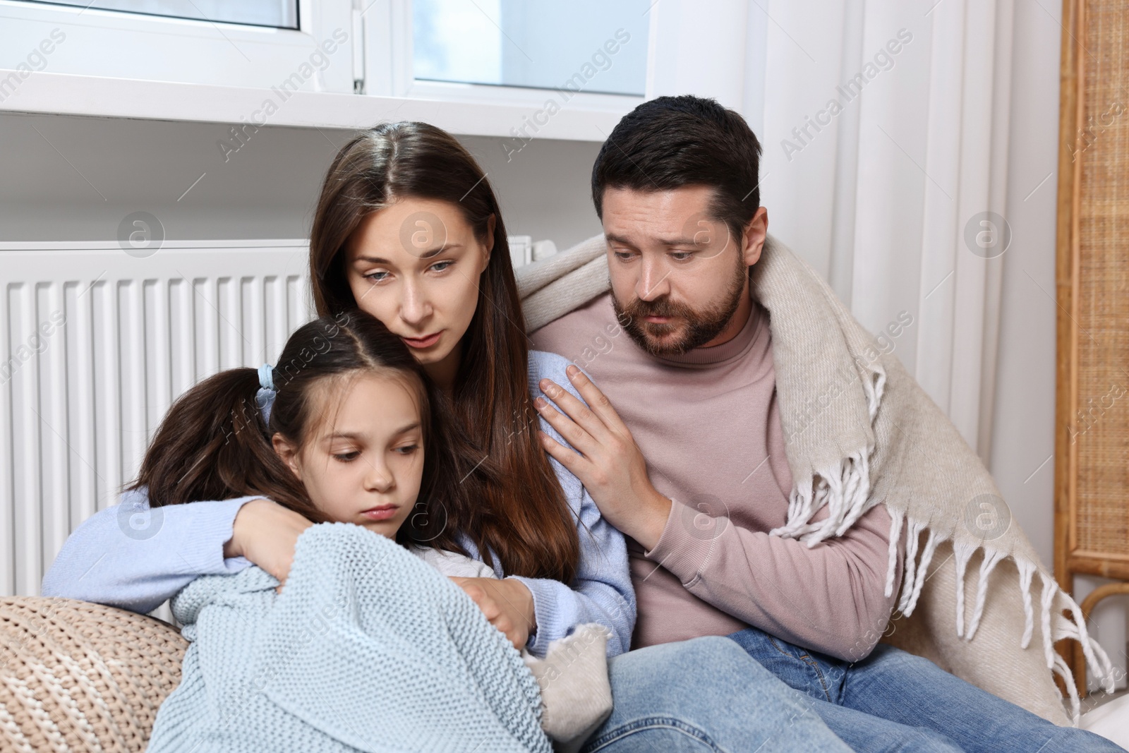 Photo of Family with blankets warming near heating radiator at home