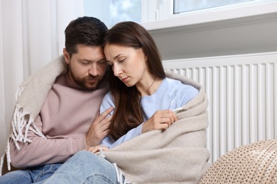 Photo of Couple with blanket warming up near heating radiator at home