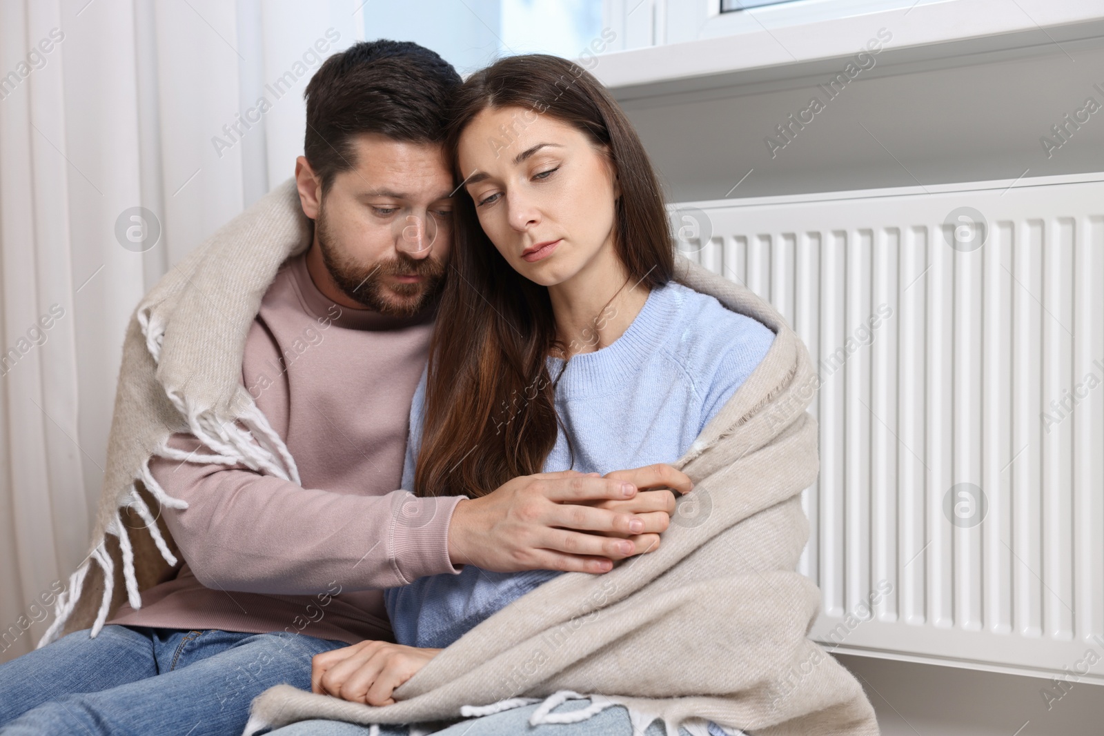 Photo of Couple with blanket warming up near heating radiator at home