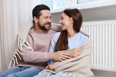 Photo of Happy couple with blanket warming near heating radiator at home