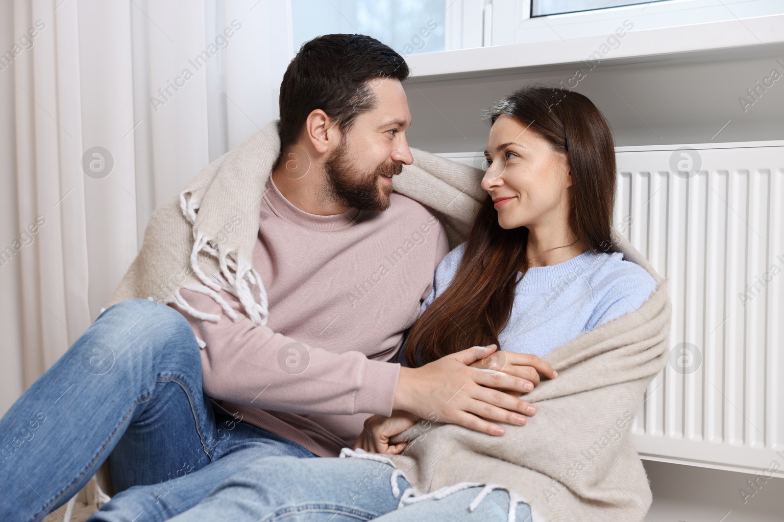 Photo of Happy couple with blanket warming near heating radiator at home