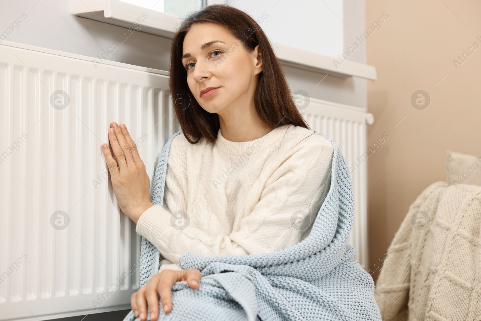 Photo of Woman with blanket warming near heating radiator at home