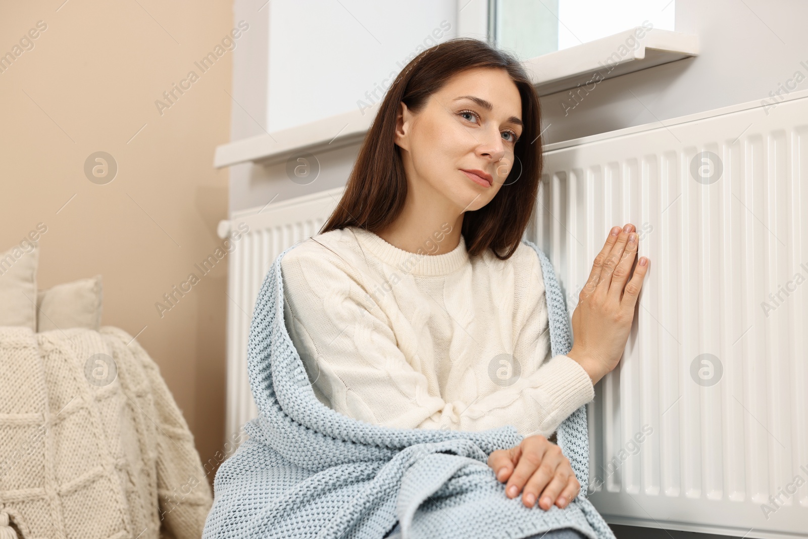 Photo of Woman with blanket warming near heating radiator at home