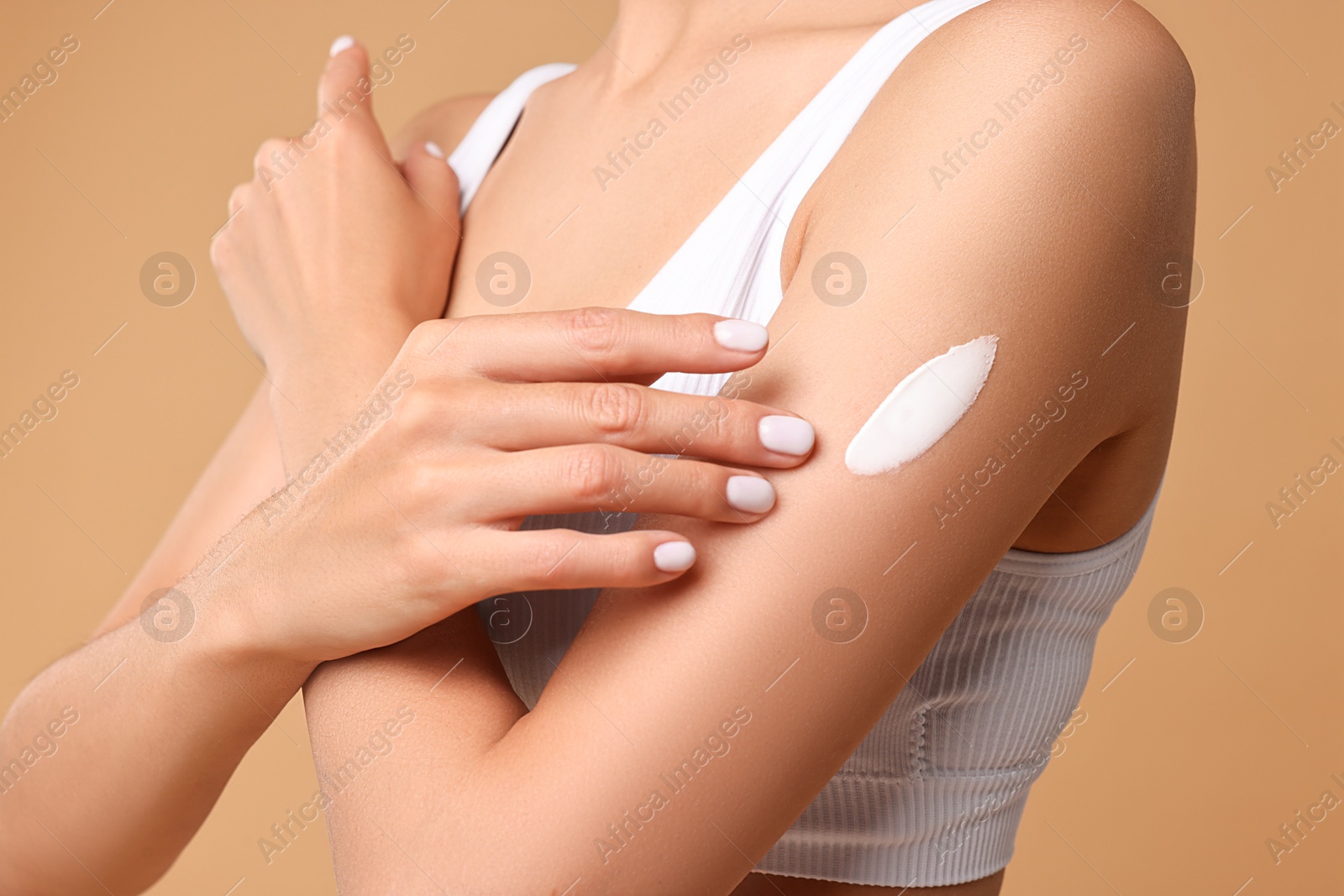 Photo of Woman applying cream onto arm on beige background, closeup. Body care