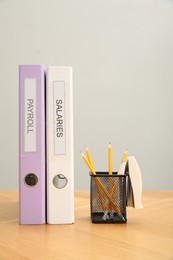 Photo of Folders with words Payroll and Salaries, holder with pencils on wooden table