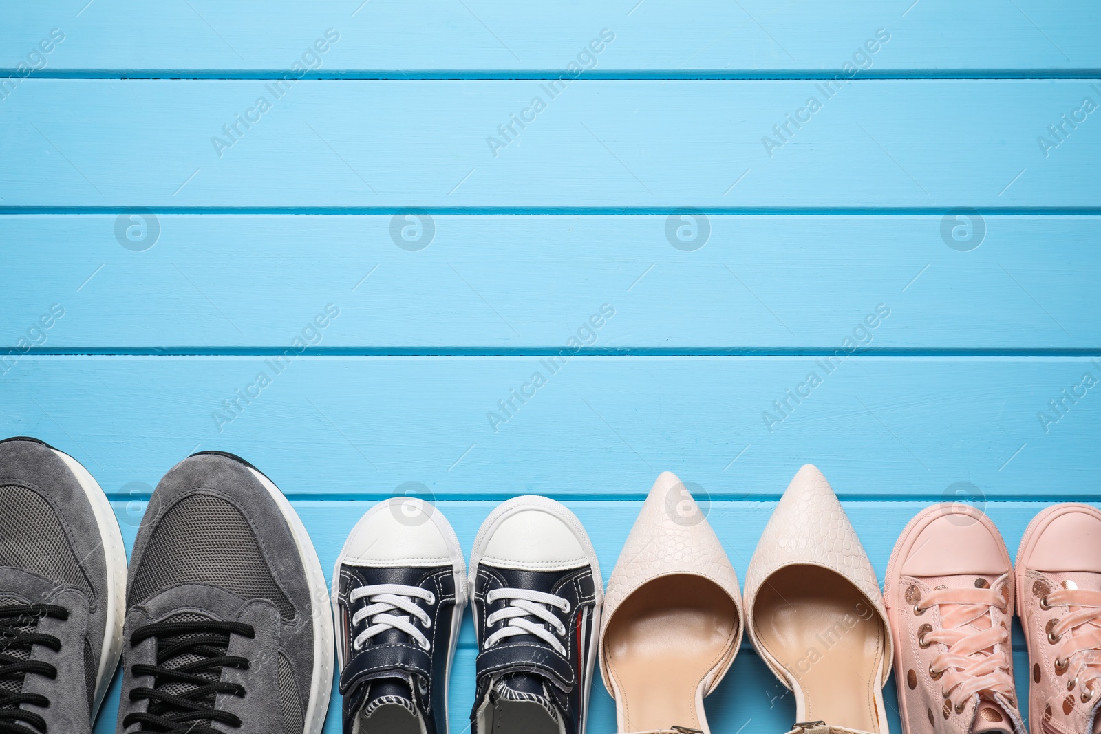 Photo of Big and small shoes on light blue wooden table, top view. Space for text