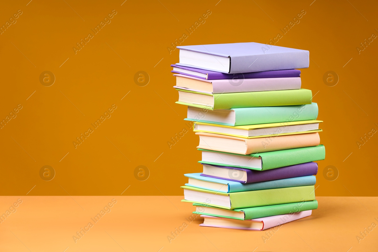 Photo of Stack of colorful books on orange background, space for text