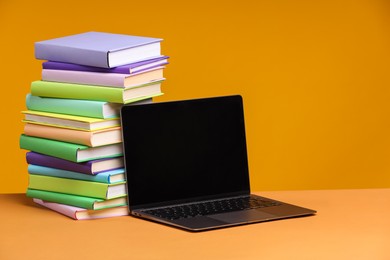 Photo of Stack of colorful books and laptop on orange background