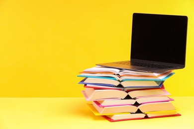 Photo of Stack of colorful books and laptop on yellow background, space for text