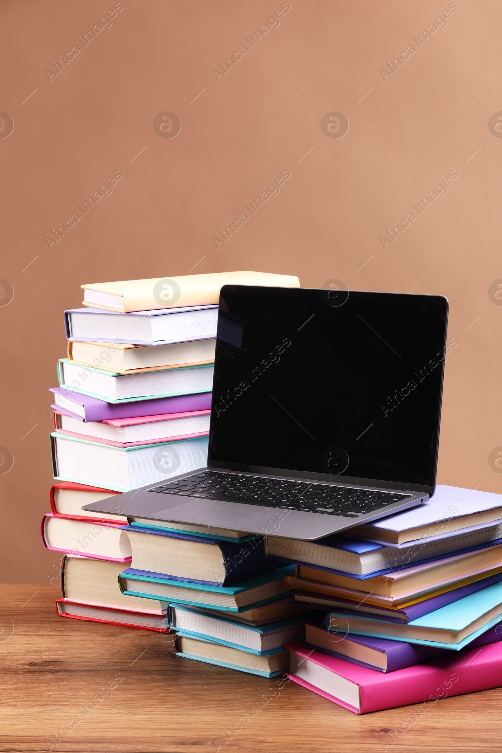 Photo of Stacks of colorful books and laptop on wooden table against light brown background