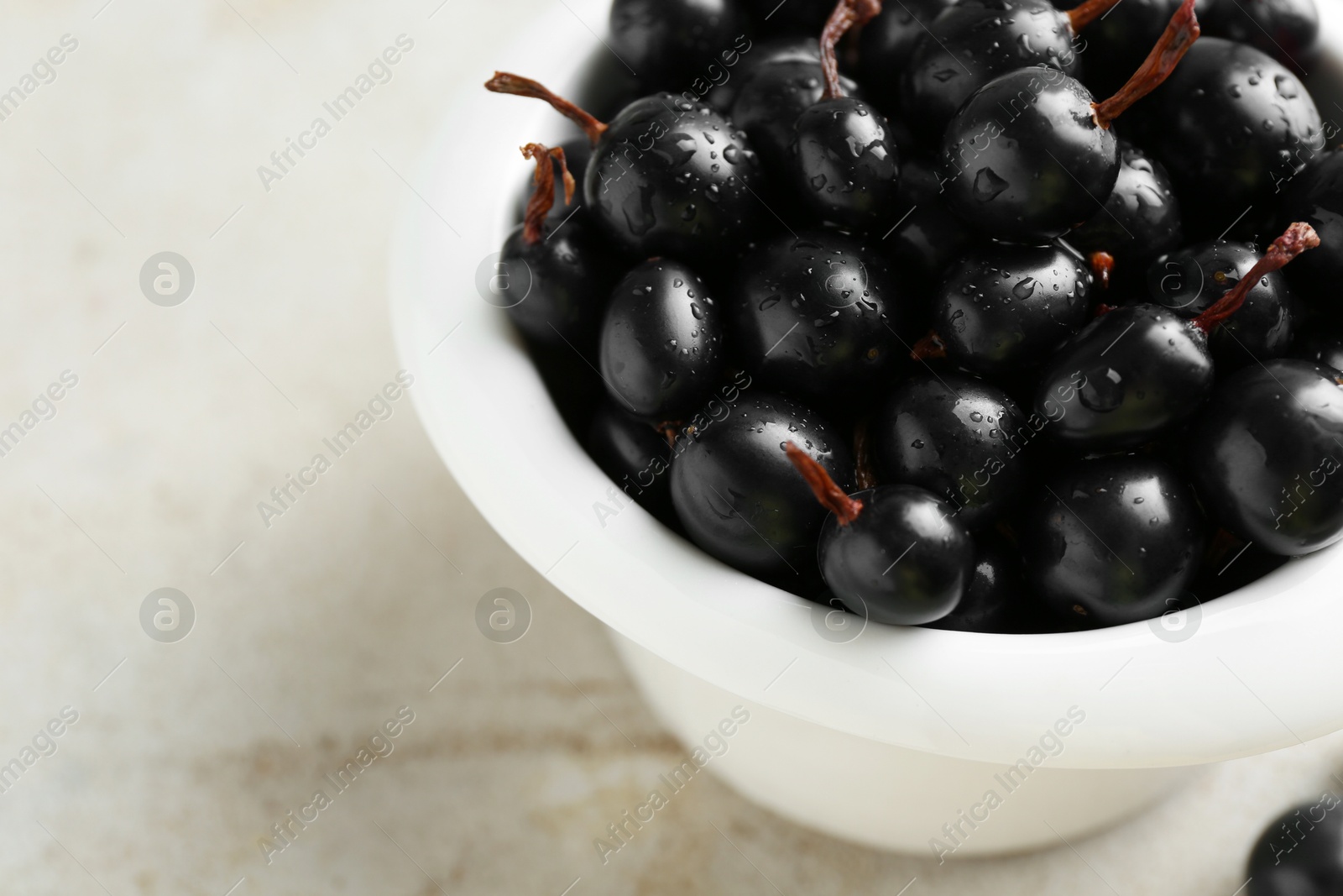 Photo of Ripe black currants in bowl on light table, closeup. Space for text