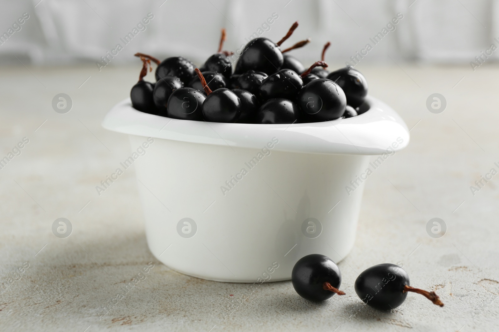 Photo of Ripe black currants in bowl on light table, closeup