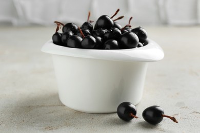 Ripe black currants in bowl on light table, closeup