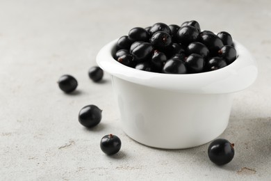 Photo of Ripe black currants in bowl on light table, closeup