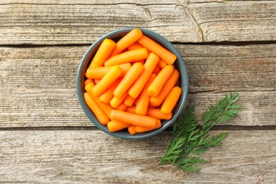 Baby carrots in bowl and green leaf on wooden table, top view