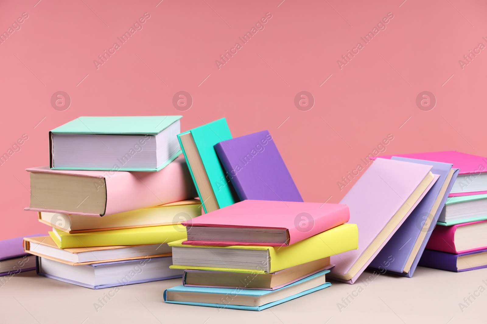 Photo of Many colorful books on beige table against pink background