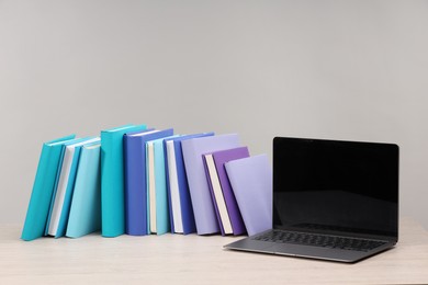 Photo of Colorful books and laptop on white wooden table against light grey background