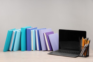 Photo of Colorful books, pencils and laptop on white wooden table against light grey background