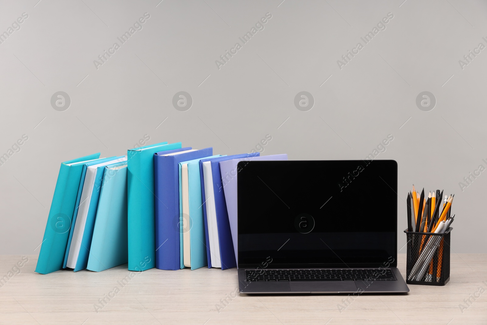 Photo of Colorful books, pencils and laptop on white wooden table against light grey background