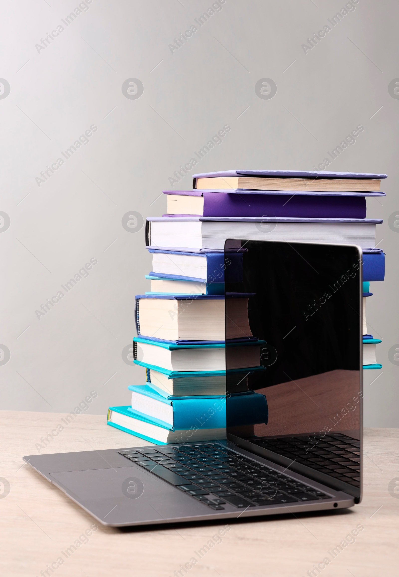 Photo of Stack of colorful books and laptop on white wooden table against light grey background