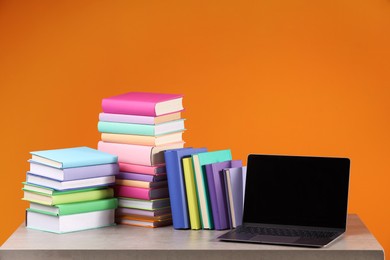 Stacks of colorful books and laptop on orange background