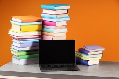 Stacks of colorful books and laptop on wooden table against orange background