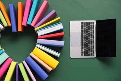 Photo of Heart made of many colorful books and laptop on green background, flat lay