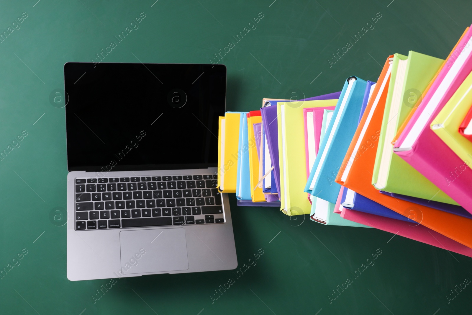 Photo of Stack of many colorful books and laptop on green background, above view