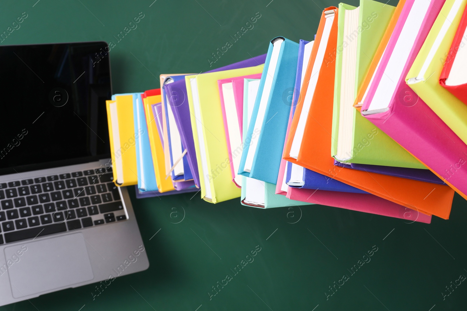 Photo of Stack of many colorful books and laptop on green background, above view