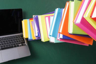 Photo of Stack of many colorful books and laptop on green background, above view