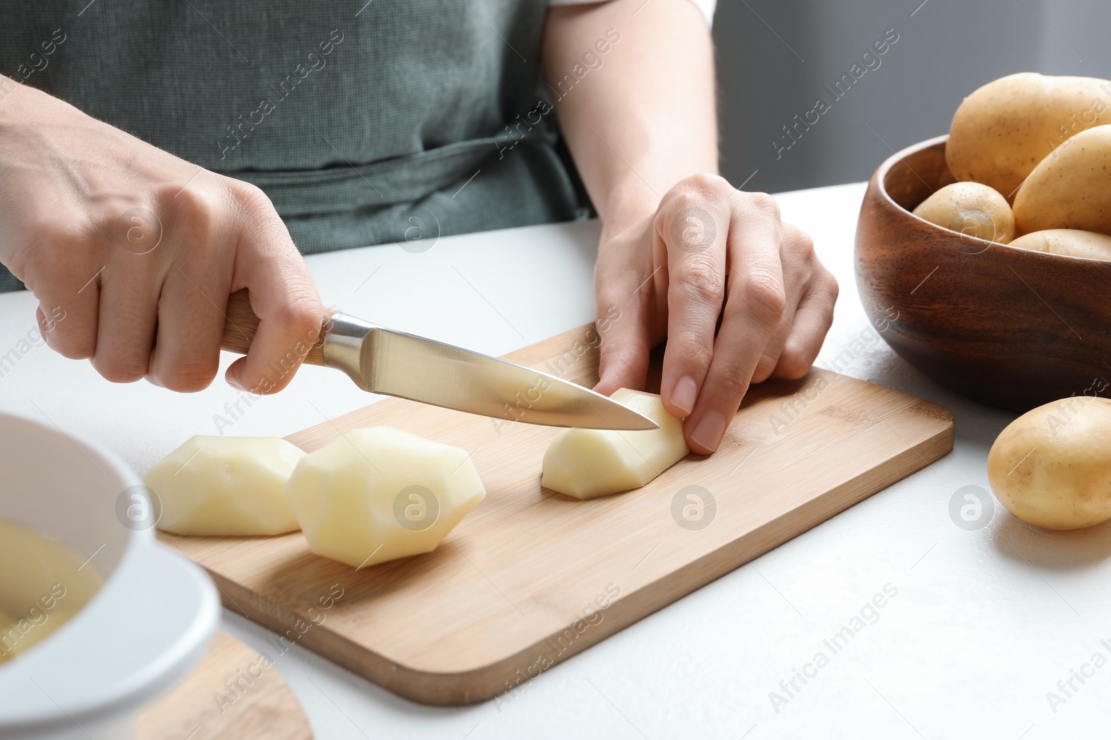 Photo of Woman cutting raw potato at white table, closeup