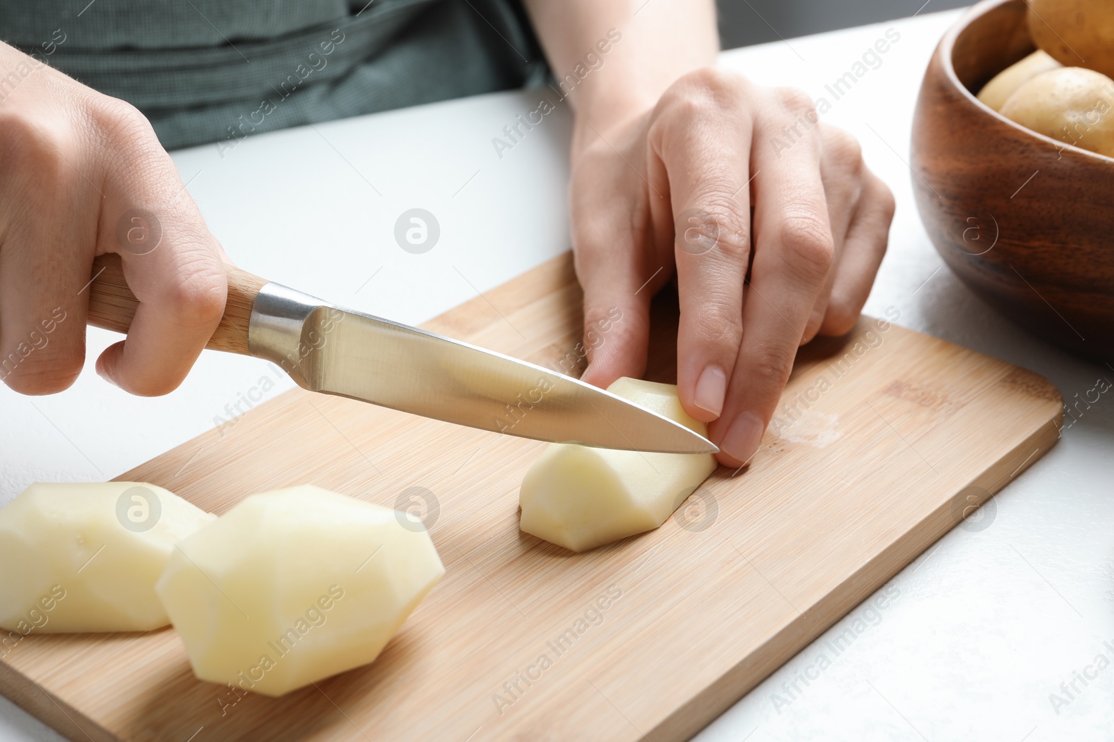 Photo of Woman cutting raw potato at white table, closeup