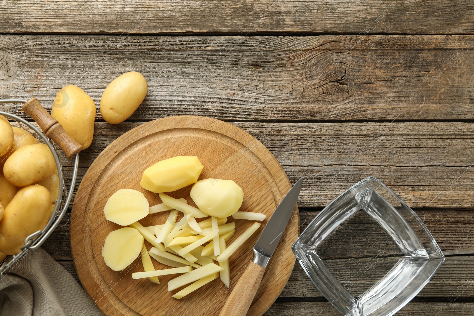 Photo of Whole and cut fresh raw potatoes near knife on wooden table, top view. Space for text