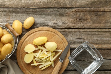 Whole and cut fresh raw potatoes near knife on wooden table, top view. Space for text