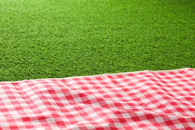 Photo of Checkered picnic tablecloth on green grass, closeup. Space for text