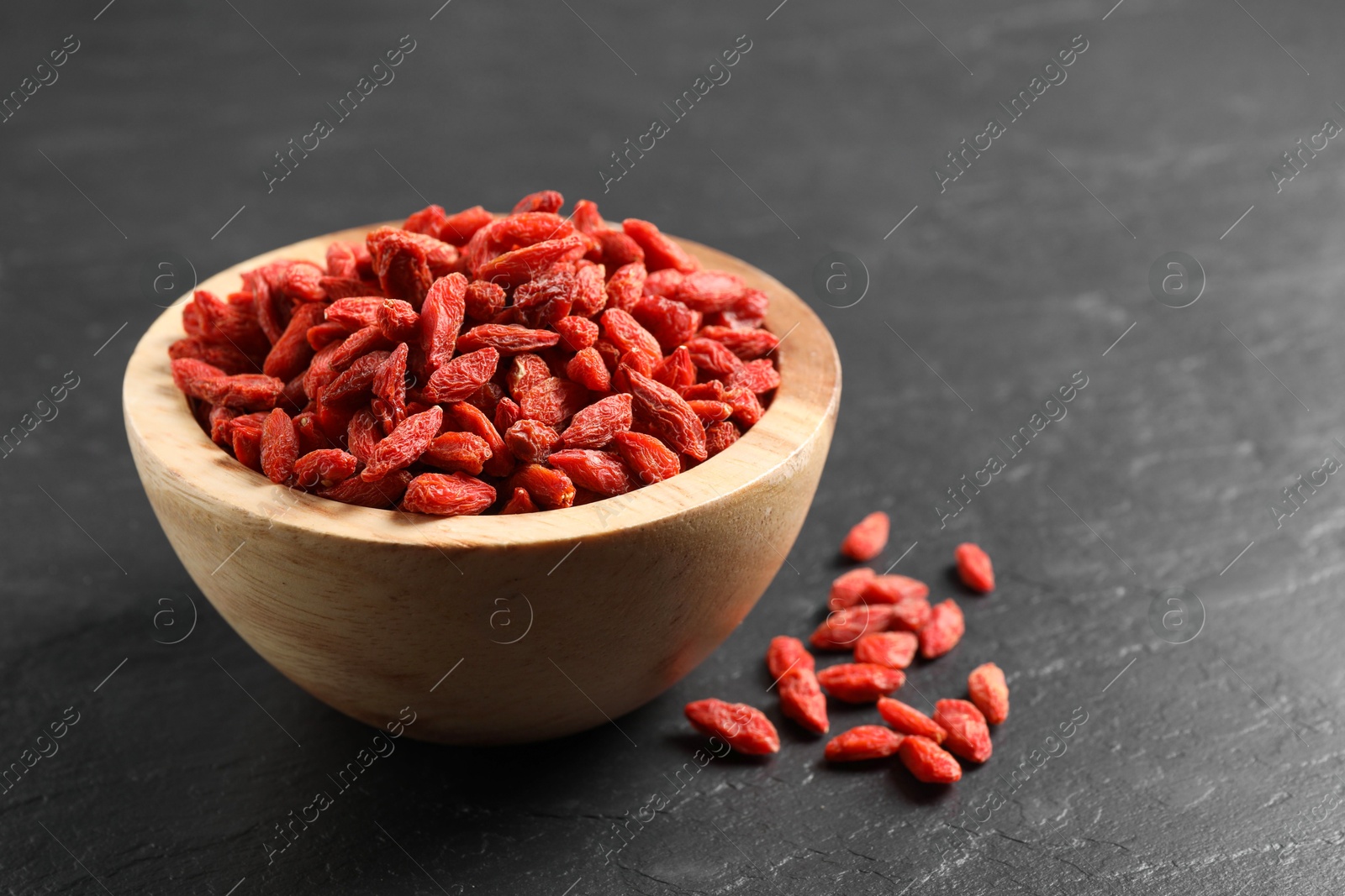 Photo of Dried goji berries in bowl on dark textured table, closeup