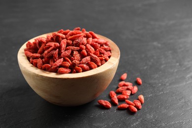 Dried goji berries in bowl on dark textured table, closeup