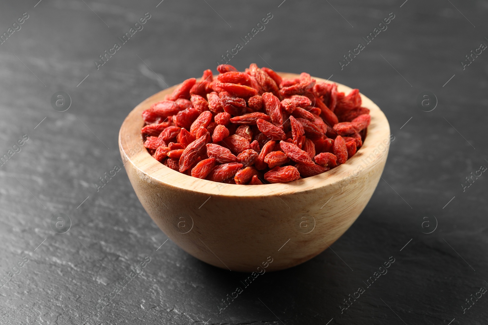 Photo of Dried goji berries in bowl on dark textured table, closeup