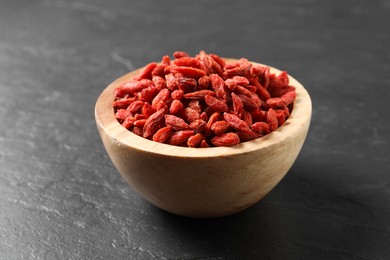 Dried goji berries in bowl on dark textured table, closeup