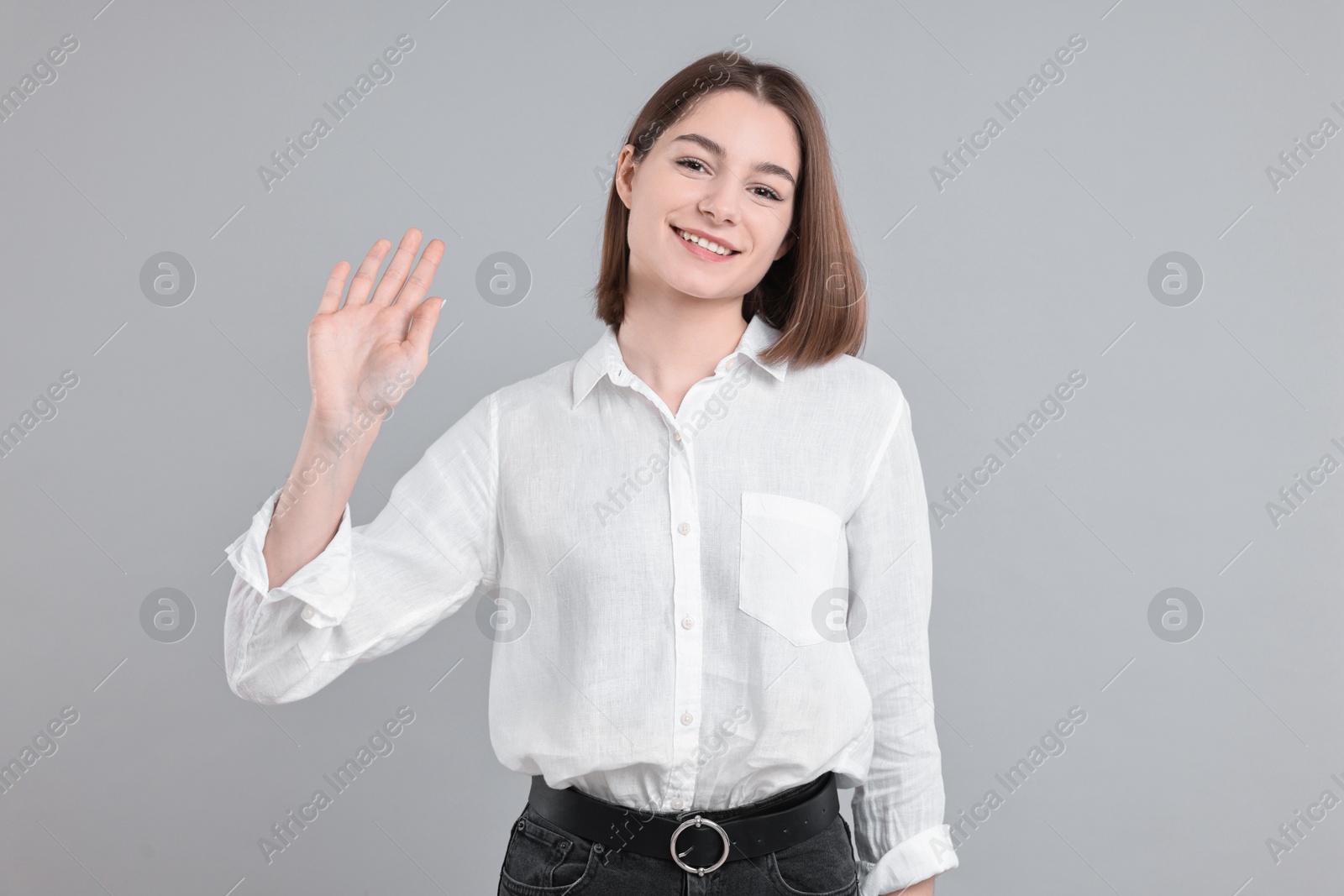 Photo of Happy teenage girl waving on gray background