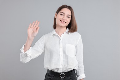 Happy teenage girl waving on gray background