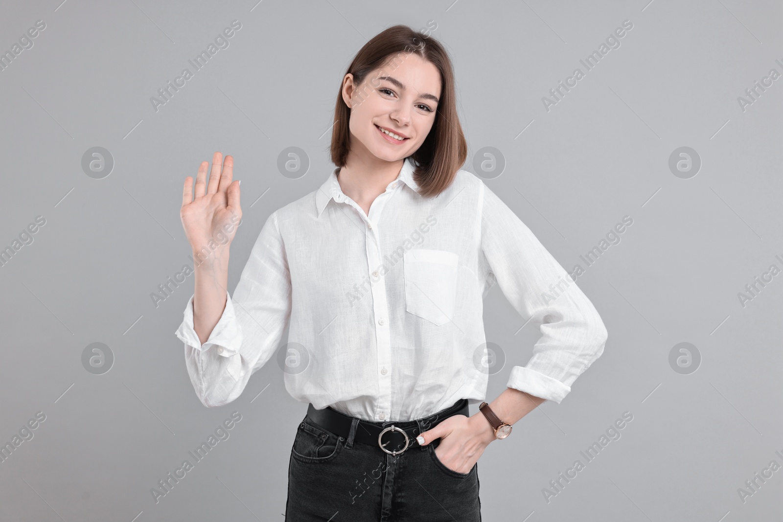 Photo of Happy teenage girl waving on gray background